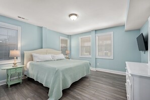 A bedroom with a bed, bedside tables, a dresser, and a TV mounted on the wall.