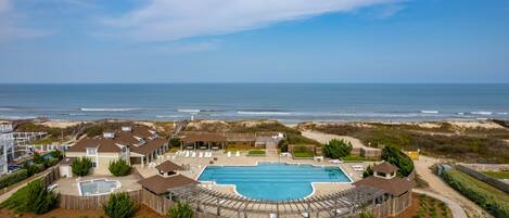 A resort with a large swimming pool, beachfront views, and a sandy beach area.