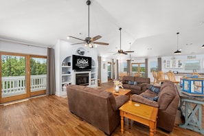 A spacious living room with a fireplace, ceiling fans, and a large window overlooking a deck.