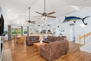 A spacious living room with a large brown sectional sofa, wooden dining table, and ceiling fans. - Heaven Sent: Oceanside, private pool, hot tub, rec room and EASY beach access! (Corolla)