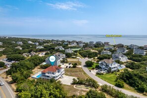 An aerial view of a coastal residential area with houses, a swimming pool, and a marked beach access point.