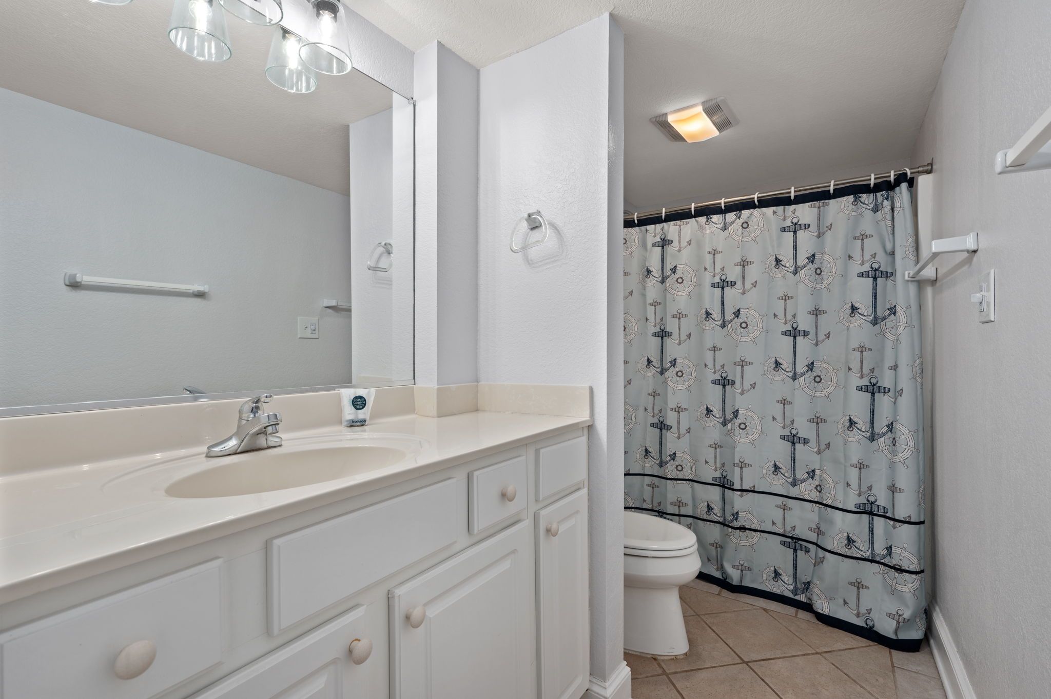 A bathroom with a large mirror, a sink, a toilet, and a shower curtain with an anchor pattern.