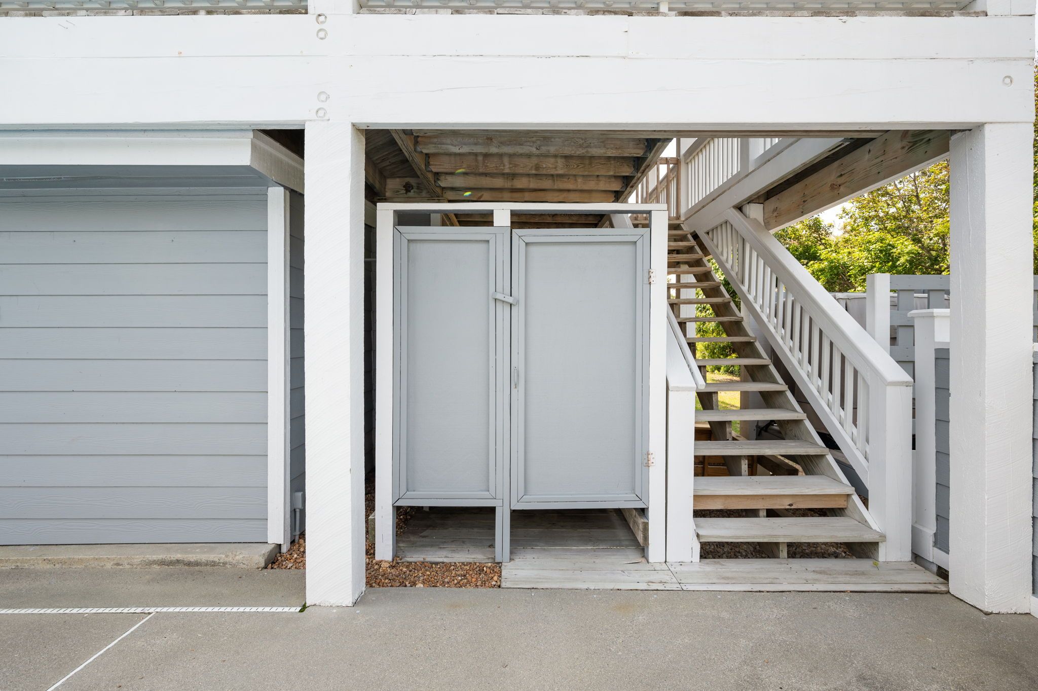 A garage with a white exterior, a set of stairs leading to a covered area, and a metal door.