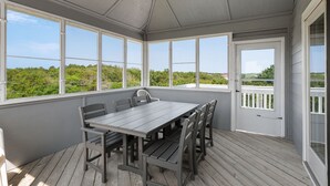 Un patio techado con mesa y sillas, ventanas amplias y vista a follaje.