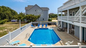 Una piscina rectangular con agua azul, rodeada de barandillas blancas y sillas reclinables azules.