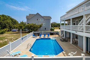 A rectangular swimming pool with blue water, surrounded by white railings and blue lounge chairs.