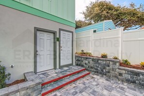 A building with two white doors, a stone staircase with red steps, and a stone wall with plants. - BRAND-NEW build! Dog Friendly! Close to Ocean! Above garage condo! (Fernandina Beach)