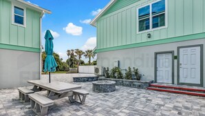 A patio area with a picnic table and benches, a stone fire pit, and a teal umbrella.