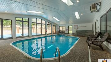 Una piscina interior con paredes de vidrio transparente, piso de baldosas y algunas sillas de descanso.
