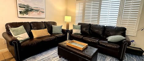 A living room with two black leather sofas, a wooden coffee table, and a blue patterned rug.