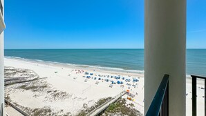 A beach view from a balcony with a clear sky, sandy beach, and umbrellas.