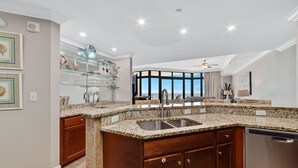A kitchen with granite countertops, a stainless steel sink, wooden cabinets, and a dishwasher.