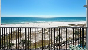 A beach view from a balcony with a railing, a pool, and lounge chairs.