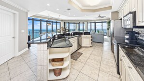 A spacious kitchen with a curved island, large windows, and a view of the ocean.