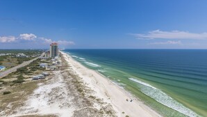 A coastal view with a beach, ocean, and a tall hotel structure.