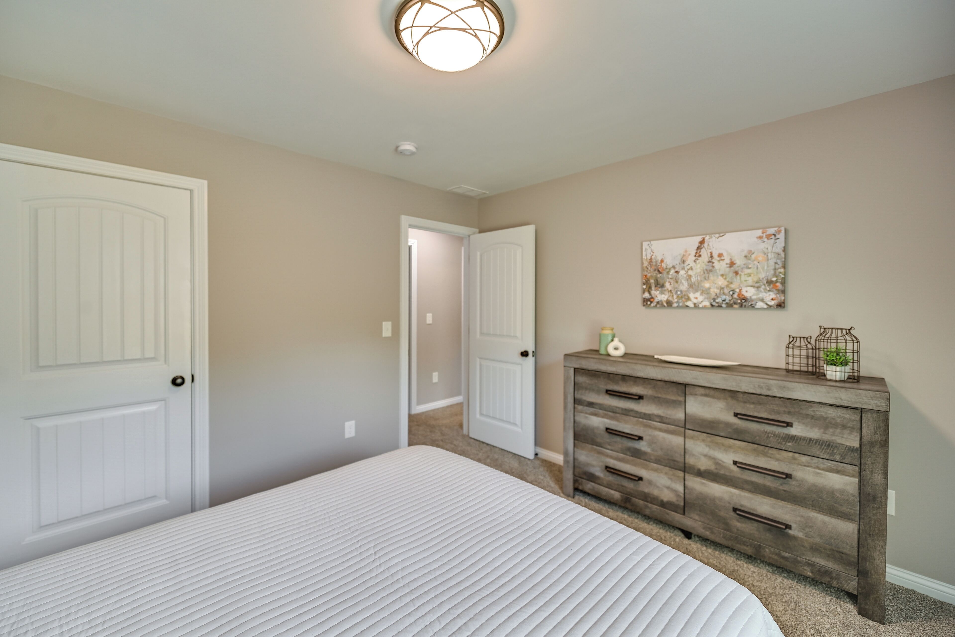 Une chambre avec deux portes blanches, une commode en bois et un tableau accroché au mur.