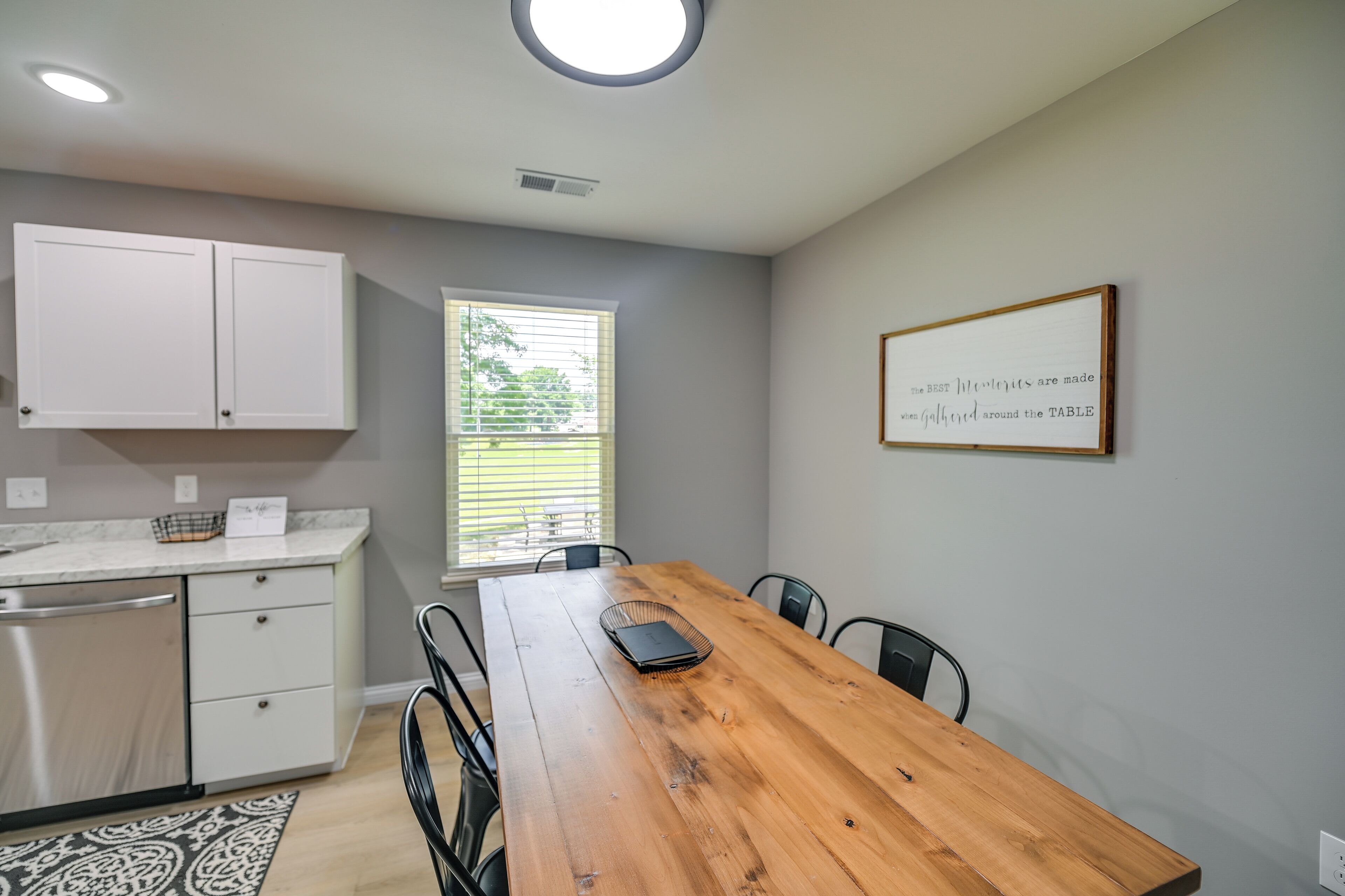A dining area with a wooden table, chairs, a white cabinet, and a framed quote on the wall.