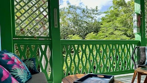 Un balcón verde con una mesa de madera, un sofá acolchado y vistas a abundante vegetación.