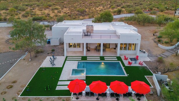 A modern building with a pool and outdoor seating, surrounded by desert vegetation and mountains in the background. - Gated Estate Near Troon N. Pool, Hot-tub, Pickleball, Frisbee Golf, Bar & Arcade (Scottsdale)