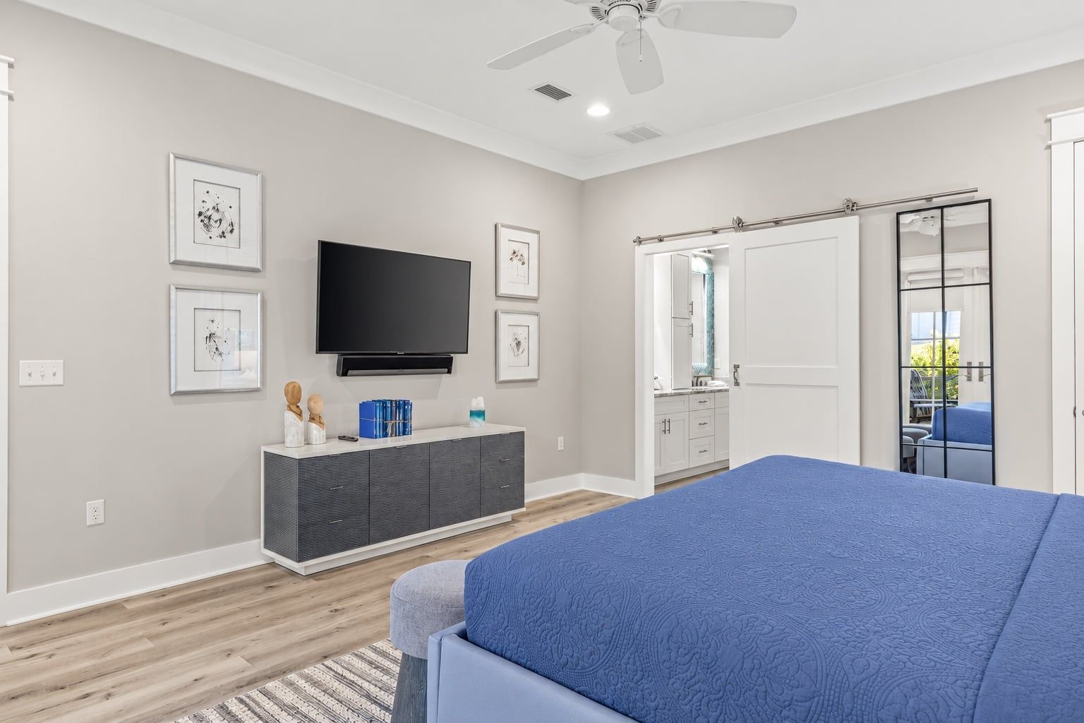 A bedroom with a bed, a TV, a dresser, a mirror, and a door leading to a balcony.