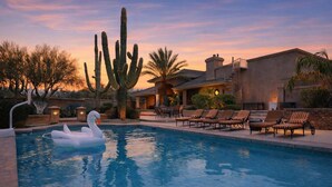 A swimming pool with swan floats, lounge chairs, and a large cactus in a desert setting. - Valley View Villa - Pool Heat Avail - Large Yard! (Scottsdale)