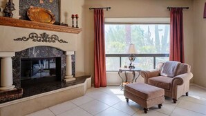 A living room with a fireplace, a sofa, a coffee table, and a window with curtains. - Valley View Villa - Pool Heat Avail - Large Yard! (Scottsdale)