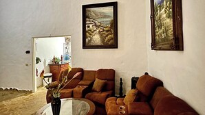 Een woonkamer met een bruine bank, een glazen salontafel en een schilderij aan de muur.
