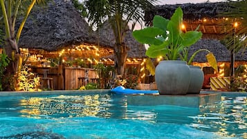 A pool with clear water, surrounded by palm trees and thatched-roof structures.