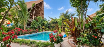 Una piscina rodeada de exuberante follaje y una estructura con techo de paja.