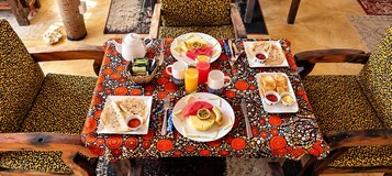 Una mesa dispuesta con diversas opciones de desayuno, como panes planos, frutas y bebidas, con un mantel estampado.
