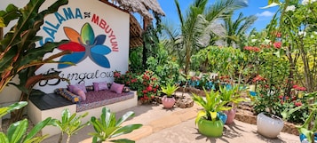 Un jardín con zona de estar, plantas en macetas y un letrero con motivos florales coloridos.