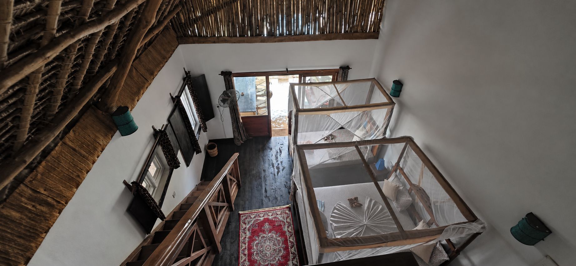 Una habitación con escalera de madera, un ventanal grande y una cama con mosquitero.