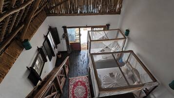 Una habitación con escalera de madera, un ventanal grande y una cama con mosquitero.