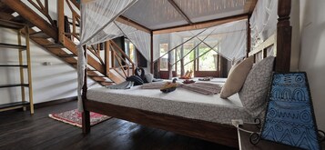 Una cama con dosel, vigas de madera, una escalera, un tapete rojo y un colgador azul con estampado.
