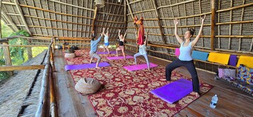 Un grupo de personas practicando yoga sobre colchonetas en una habitación con techo de paja y piso de madera.