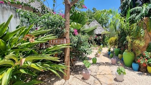 A garden with a sign reading "KARIBUNI," surrounded by various potted plants and a thatched-roof structure. - Salama & Mbuyuni Bungalows (Matemwe)