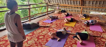 Un grupo de personas practicando yoga sobre colchonetas en una habitación con alfombra estampada y techo de paja.