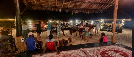 A beachside gathering with a thatched-roof structure, tables, and chairs.