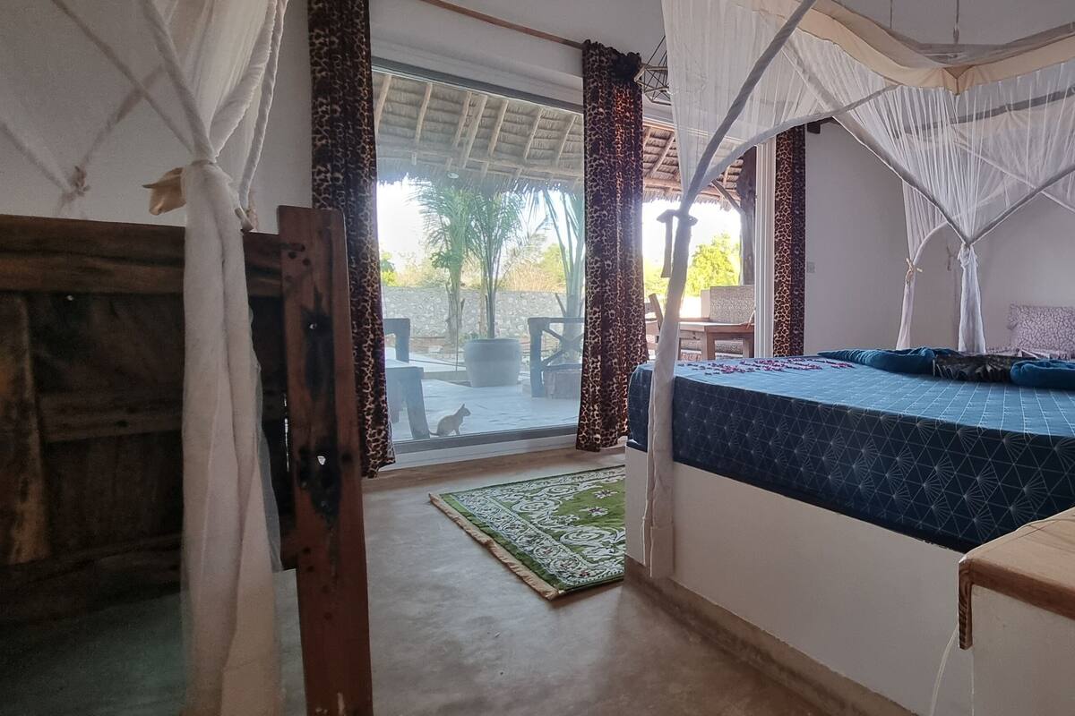 Habitació amb un llit sota una estança, vista cap a l'exterior i un banc de fusta amb coixins.