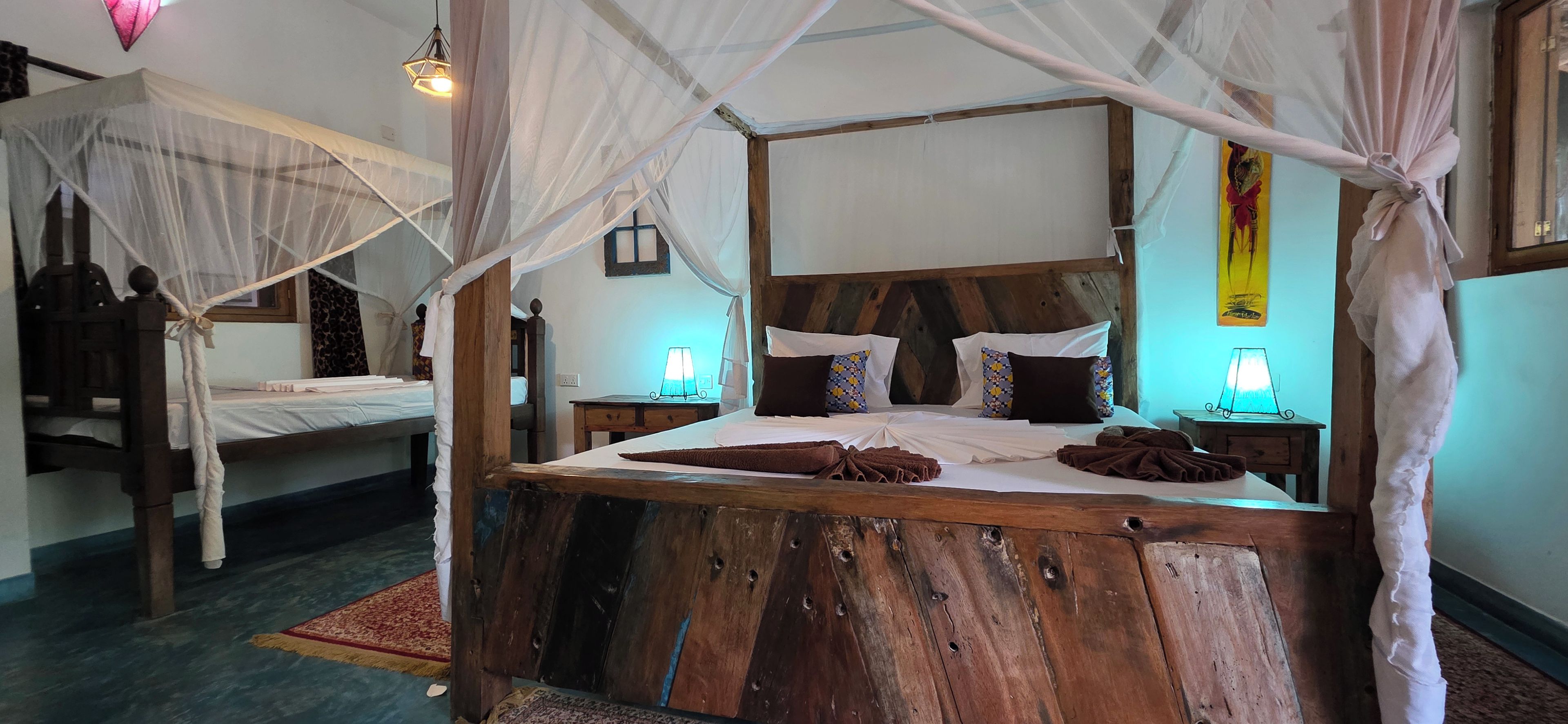 Een bed met houten frame en hemel, een nachtkastje met lamp, en een nachtstandaard met lamp.