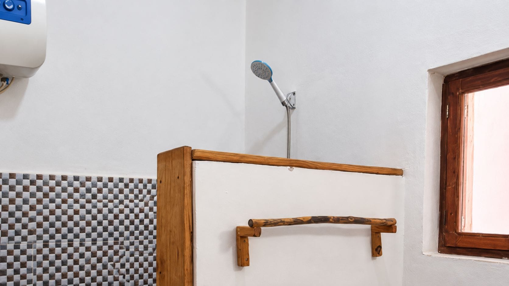 Un área de ducha con estructura de madera, un cabezal de ducha y pared de baldosas a cuadros.