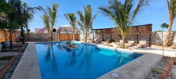 Una piscina rectangular con sillas de descanso y palmeras.