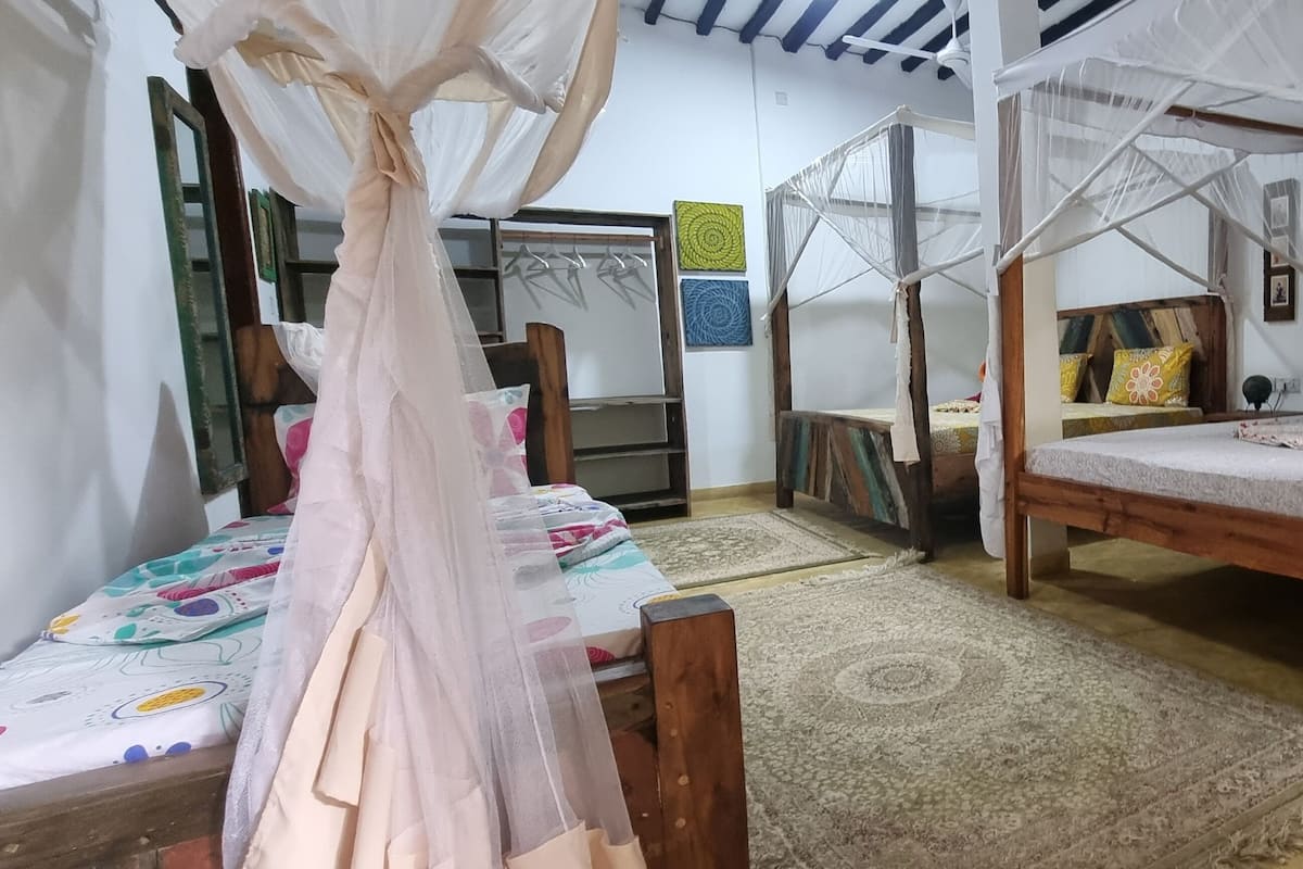 Habitació amb un llit de fusta, una taula petita i una cadira. Hi ha una mosquitera sobre el llit.
