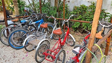 A collection of bicycles parked in a garden area with a concrete wall and greenery in the background.