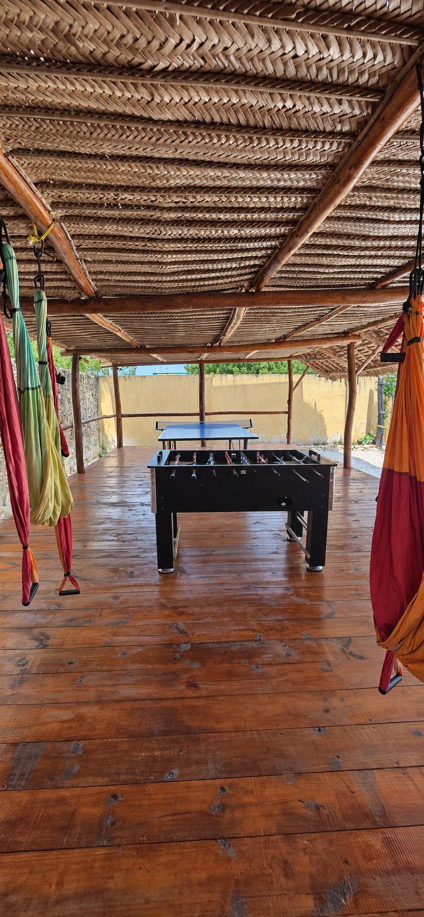 Un espacio interior con piso de madera, una mesa de futbolín y paraguas colgantes.