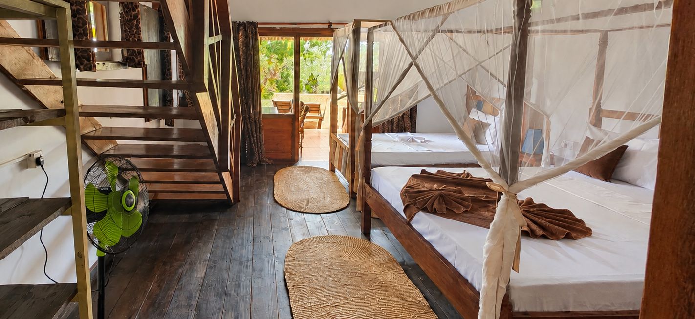 Una habitación con escalera de madera, una cama con mosquitero y un ventilador.