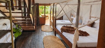 Una habitación con escalera de madera, una cama con mosquitero y un ventilador.