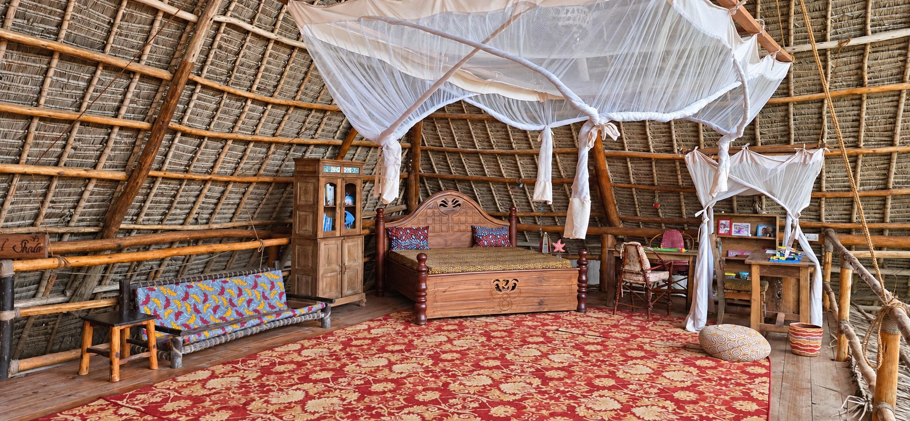 A room with a thatched roof, a wooden bed with a canopy, a small cabinet, and a colorful bench.
