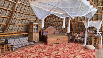 A room with a thatched roof, a wooden bed with a canopy, a small cabinet, and a colorful bench.