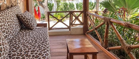 A wooden deck with a sofa and table, surrounded by a wooden railing and lush greenery.